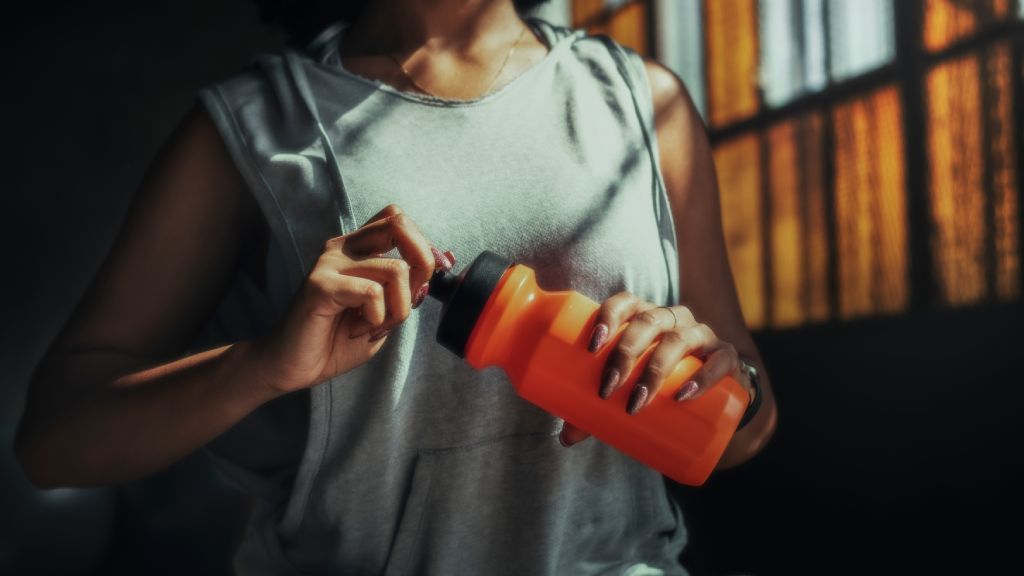 A woman wearing a sleeveless exercise top hydrates during her workout